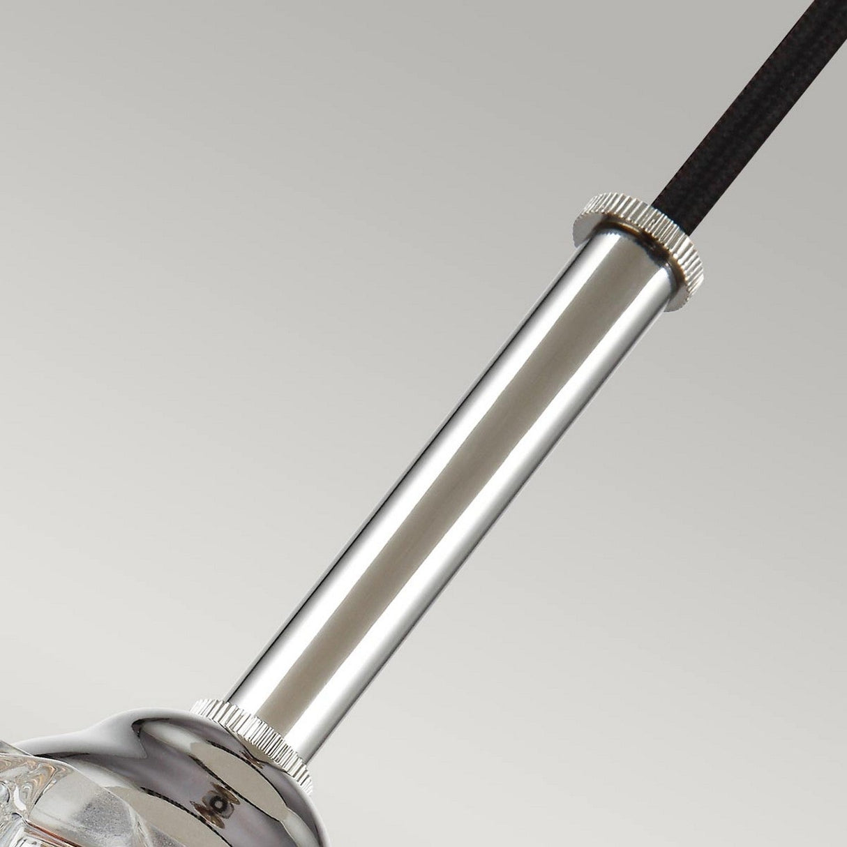 Here is a close-up of the Rubin 1 Light Mini Pendant, featuring a sleek cylindrical form with ridged edges and a polished nickel finish, attached to a black cable. The background is a simple, light gray color.