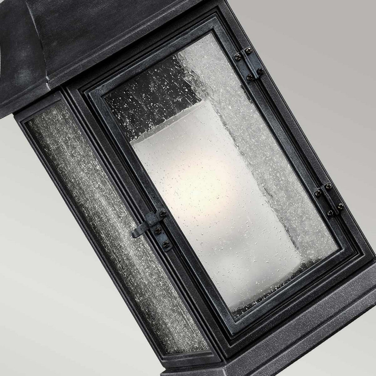 A close-up of a black-framed window set against a grey background captures raindrops on the glass, partially obscuring the view. The surrounding frame, similar to that of the Shepherd 1 Light Outdoor Large Wall Lantern in Dark Weathered Zinc, features an angled design that enhances its sleek aesthetic.