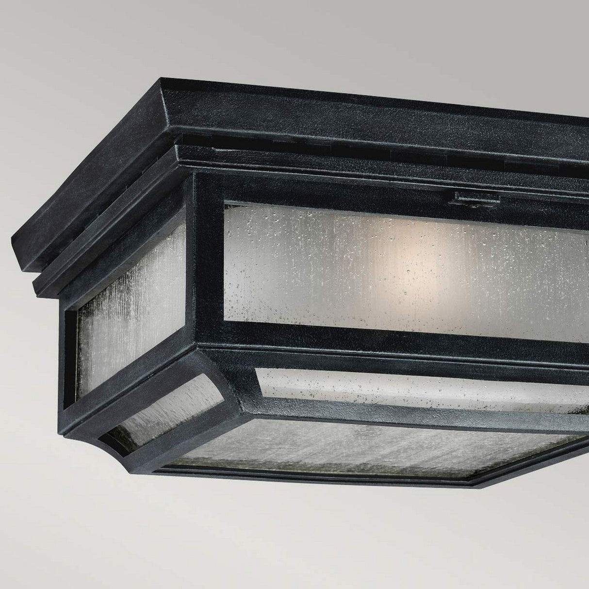 Introducing the Shepherd 2 Light Outdoor Flush in Dark Weathered Zinc: This rectangular ceiling light fixture features textured glass panels and a vintage charm. Its straightforward, industrial design is weather-resistant, making it perfect for outdoor use. The glass softly diffuses the interior light, evoking the gentle glow of an outdoor lantern.