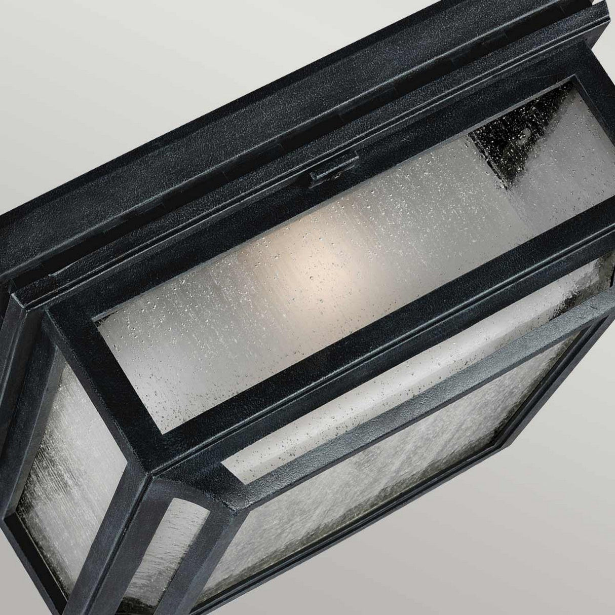 The Shepherd 2 Light Outdoor Flush, in Dark Weathered Zinc, showcases clear textured glass panels and a black metal frame. The light within casts a soft, diffused glow, imparting a vintage charm to your exterior decor.