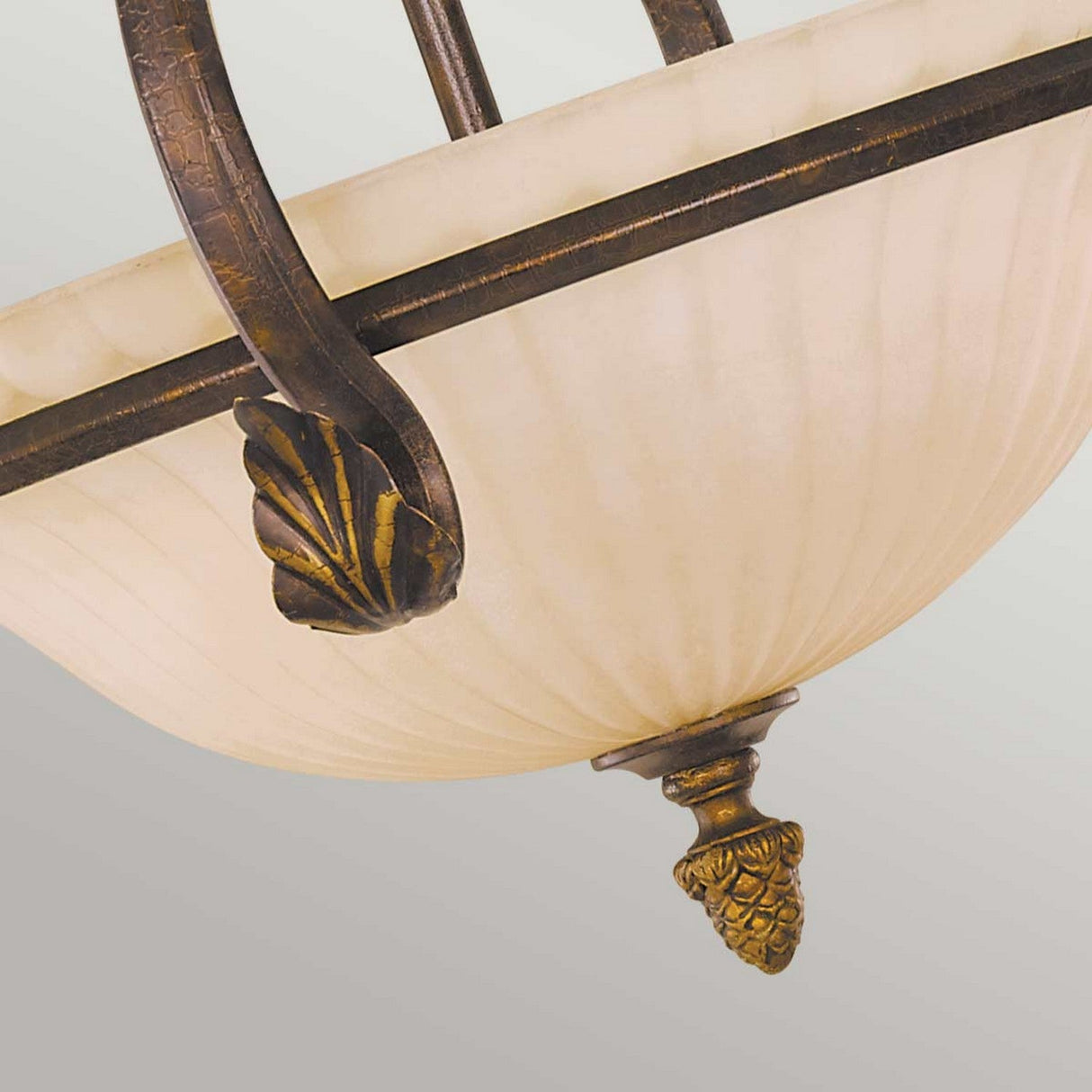 A detailed view of the Sonoma Valley 3 Light Semi Flush showcases its bowl-shaped, cream-colored glass shade, accented with intricate bronze designs featuring leaf motifs. It embodies the charm of French Country antiques and exudes an elegant vintage style against a neutral background.