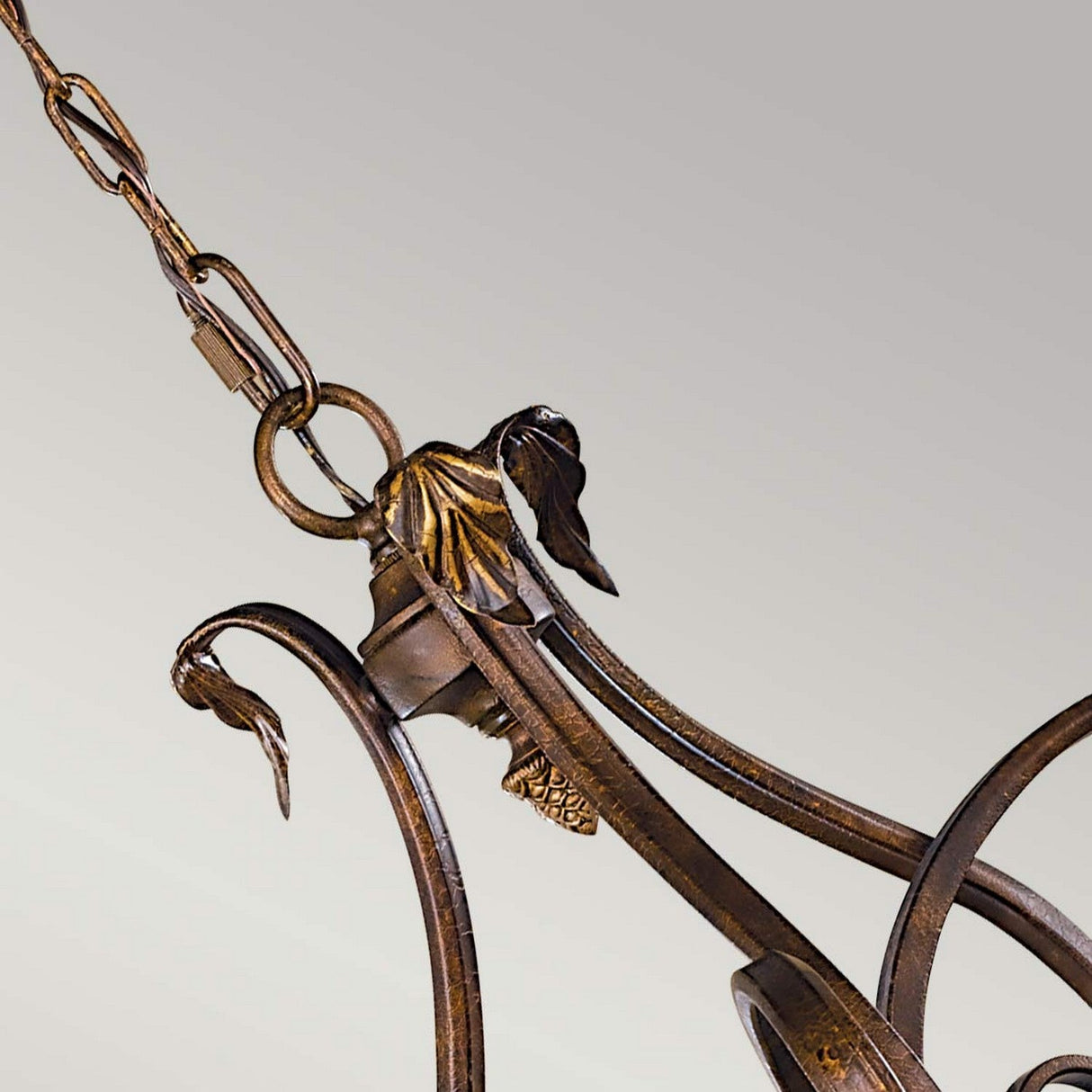 Close-up of the Sonoma Valley 3 Light Chandelier in Cream/Bronze, featuring intricate leaf designs and curved metalwork that exude rustic elegance. Reminiscent of French Country antiques, the visible chain suggests it hangs from a ceiling, while the plain background highlights its exquisite craftsmanship.