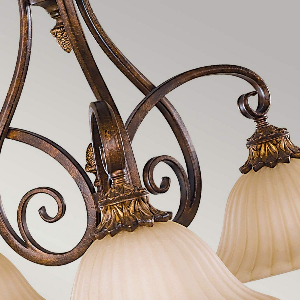 A close-up of the Sonoma Valley 3 Light Chandelier - Cream/Bronze reveals its rustic elegance, featuring intricate metal curls and bronze detailing. The chandelier boasts three bell-shaped frosted glass shades adorned with floral accents, reflecting the charm of French Country antiques against a neutral backdrop.