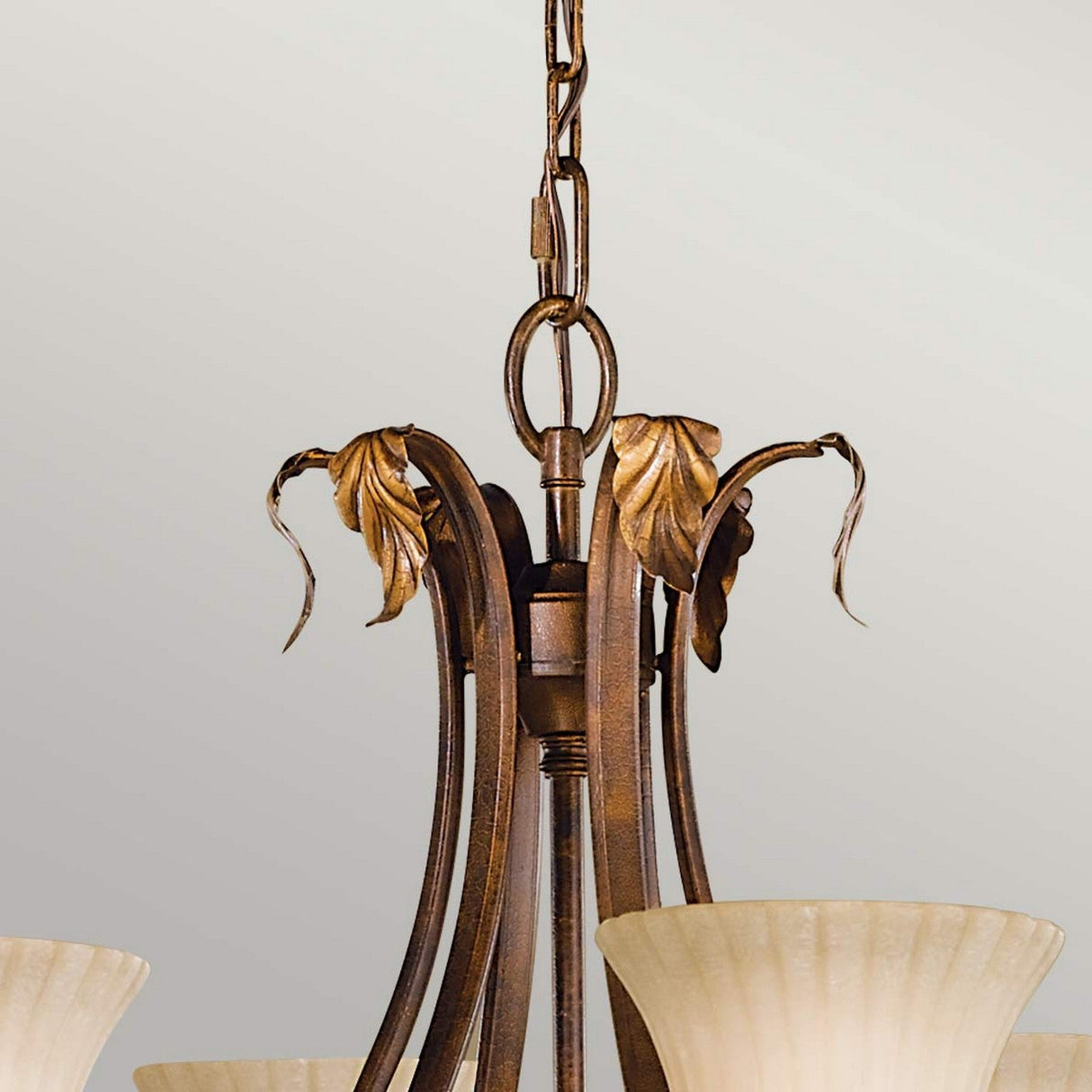 A close-up of the Sonoma Valley 6 Light Chandelier - Cream/Bronze highlights its bronze finish and decorative leaf accents. Resembling French Country antiques, this fixture features opal glass shades and elegantly suspends from a chain.