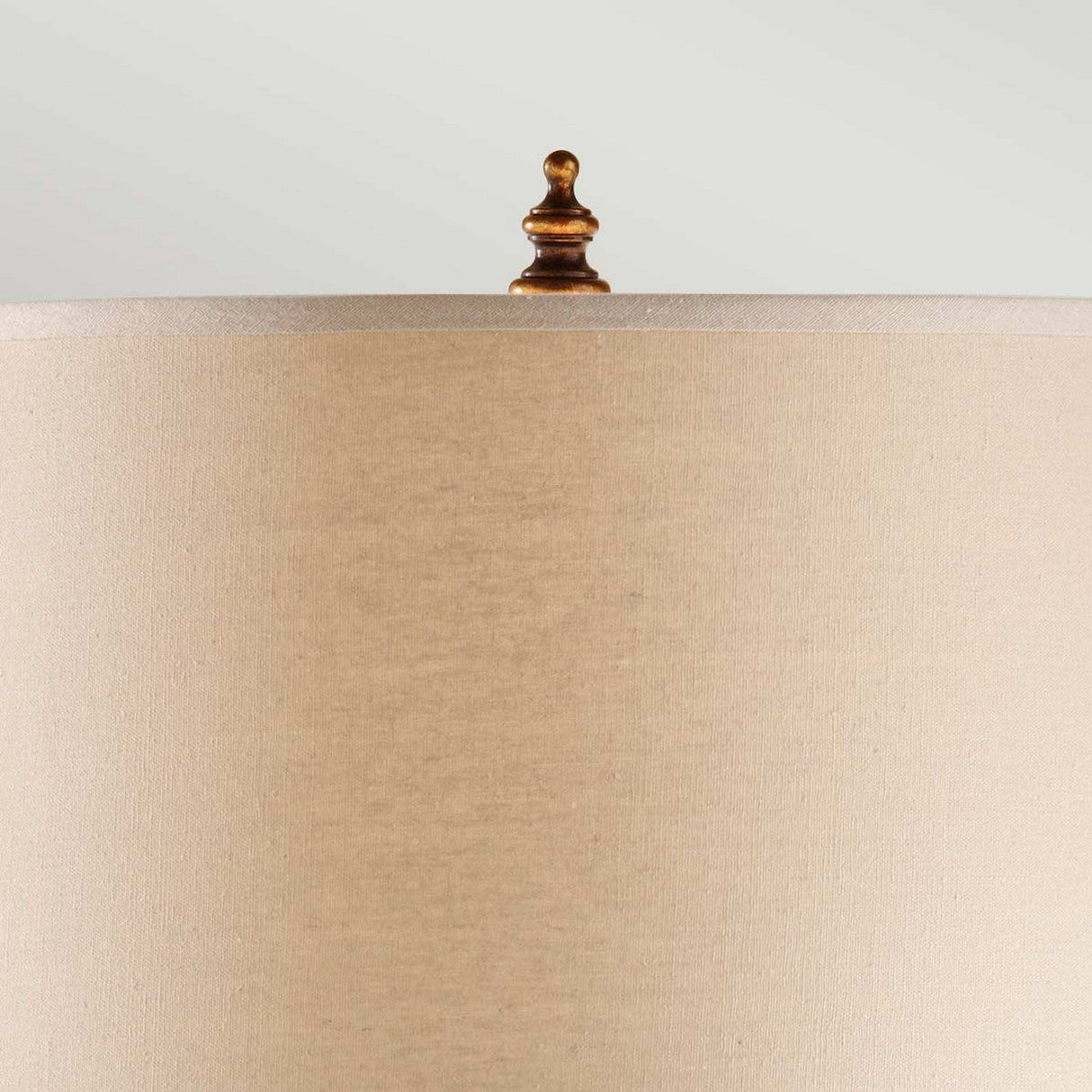 The Spencer 1 Light Table Lamp in Firenze Gold showcases a beige lampshade with a carved spindle-like finial, elegantly resting on a Dark Walnut base. Its sophisticated design is highlighted against a light gray backdrop.
