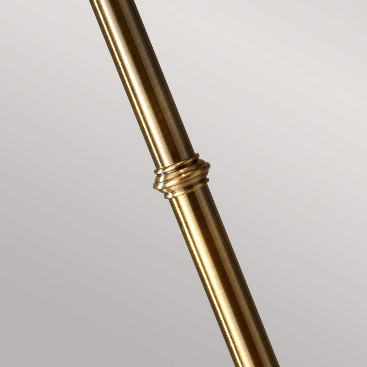 Close-up of the Stateroom 2 Light Floor Lamp - Brass, showcasing a brass-colored rod with a metallic surface and a decorative ring in the center. The rod features a brass finish and is positioned diagonally against a neutral background.