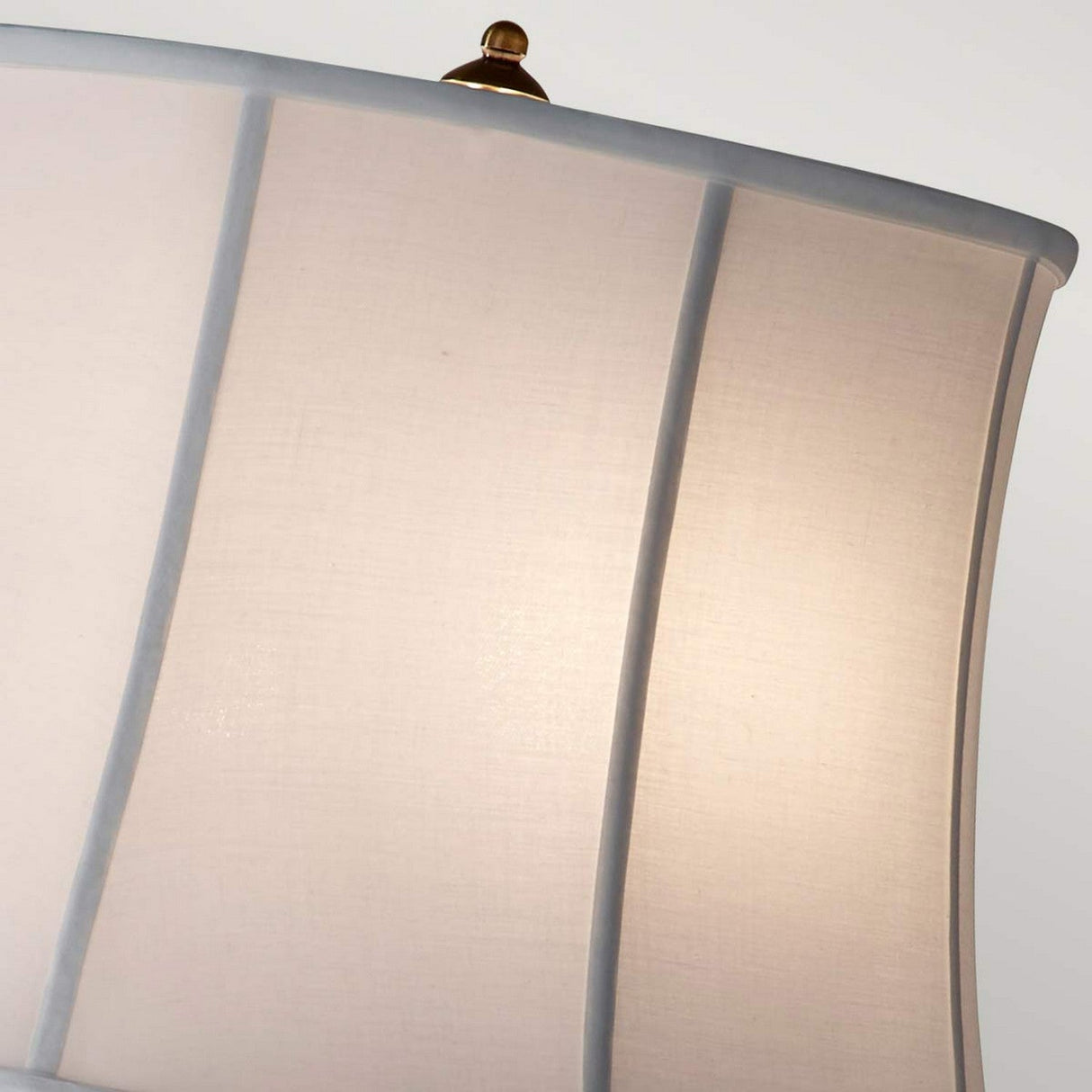 Close-up of the Stateroom 2 Light Floor Lamp in brass, featuring a soft, white fabric shade. The rounded edges and vertical seams are gently illuminated, casting a warm glow. A small golden finial adds elegance against a neutral background, while the brass finish beautifully complements its dual light feature.