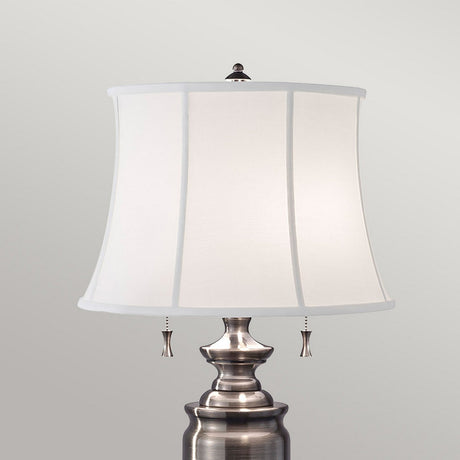 The Stateroom 2 Light Table Lamp - Antique Nickel, with its sleek metal base and polished finish, features a white cotton linen lampshade. Its two small pull chains and classic design provide versatile lighting against a plain light background.