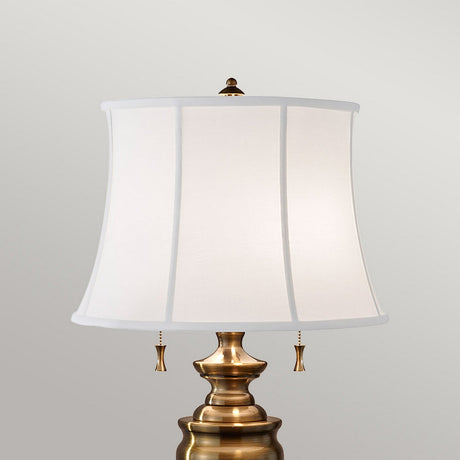 The Stateroom 2 Light Table Lamp - Brass showcases a white, rectangular lampshade set against a simple gray background. Featuring two pull chains and an ornamental finial atop, it's an elegant touch to enhance any home decor lighting arrangement.