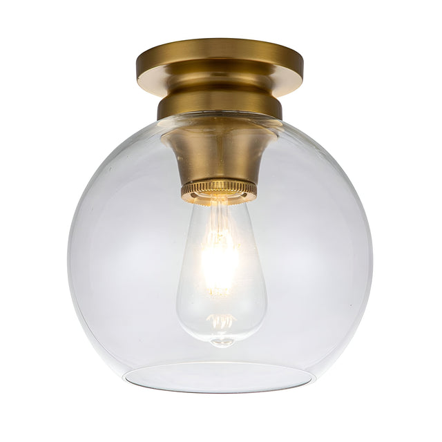The Tabby 1 Light Flush - Burnished Brass features a burnished brass finish and a clear glass shade. Inside, an exposed bulb casts a warm glow against the white background, creating an inviting ambiance.