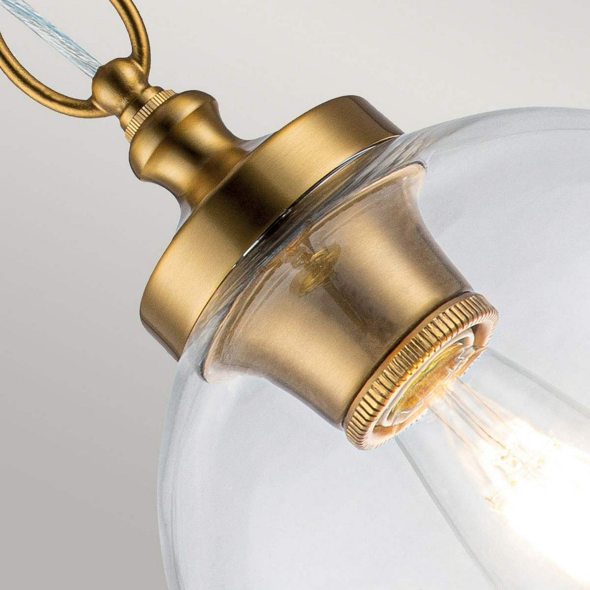 Take a closer look at the Tabby 1 Light Mini Pendant in Burnished Brass, featuring a vintage-style design. The clear glass shade allows the illuminated bulb inside to emit a warm glow. Its minimalist design is elegantly suspended by a decorative metal loop at the top, adding to its timeless appeal.