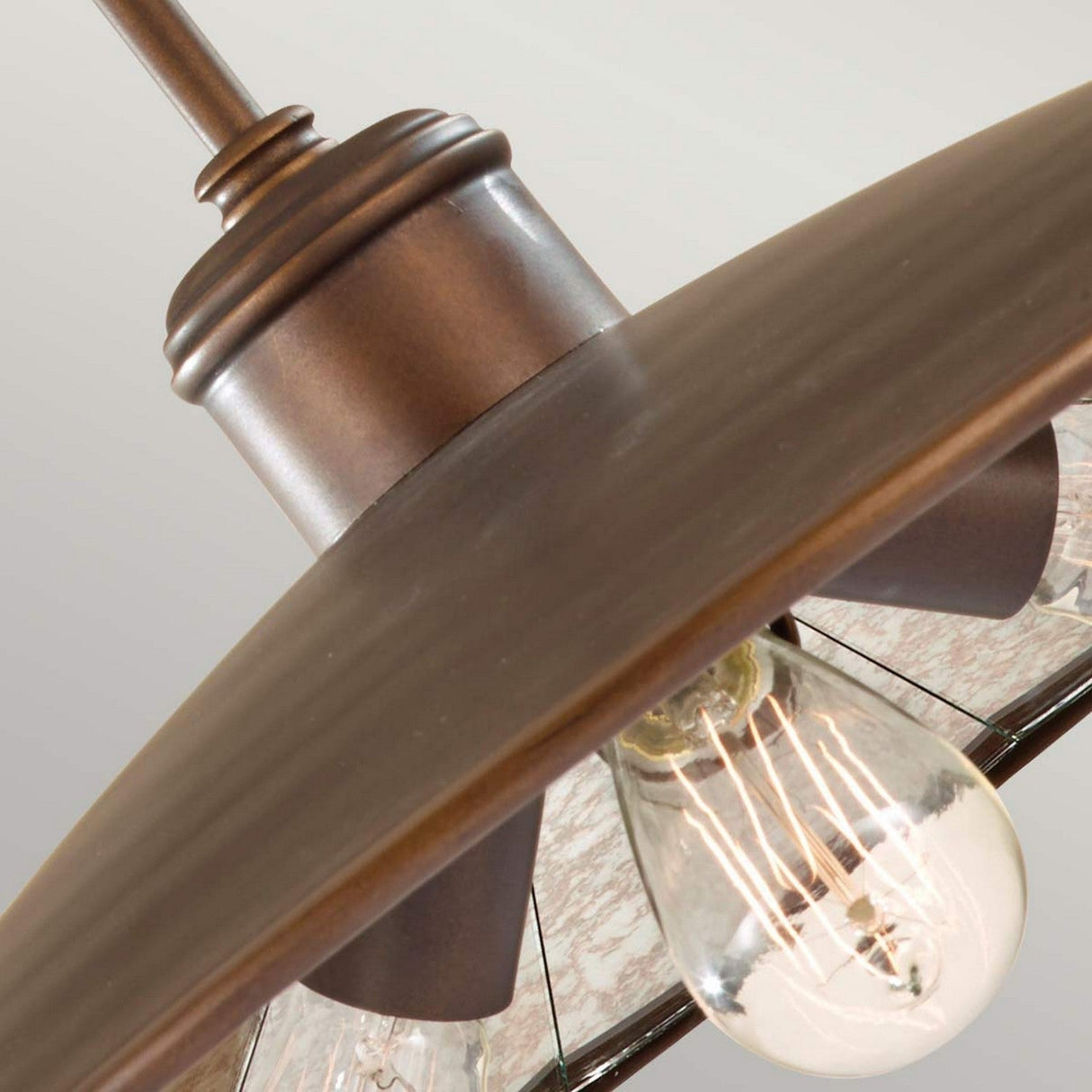 Close-up of the Urban Renewal 3 Light Large Pendant - Bronze featuring a vintage-style exposed Edison bulb. The fixture boasts a metal shade with a bronze finish, lending a warm, industrial appearance. The background is softly blurred.
