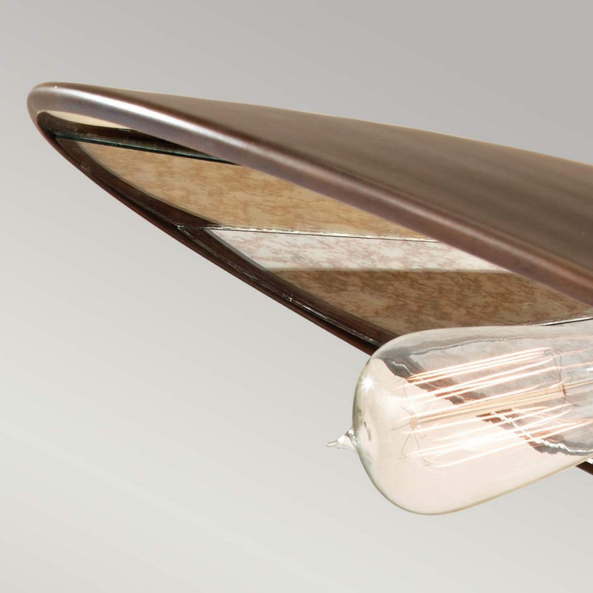 A close-up of the Urban Renewal 3 Light Large Pendant in Bronze is paired with a wooden airplane wing against a neutral background, merging aviation elements with industrial design.