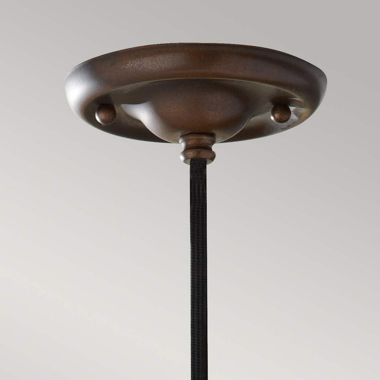 A detailed view of the Urban Renewal 1 Light Pendant in bronze features an industrial pendant light design with a dark cord hanging below. The ceiling canopy showcases a smooth, rounded shape and matte finish against a plain, light gray background. An Edison-style bulb provides just the right touch of nostalgia.