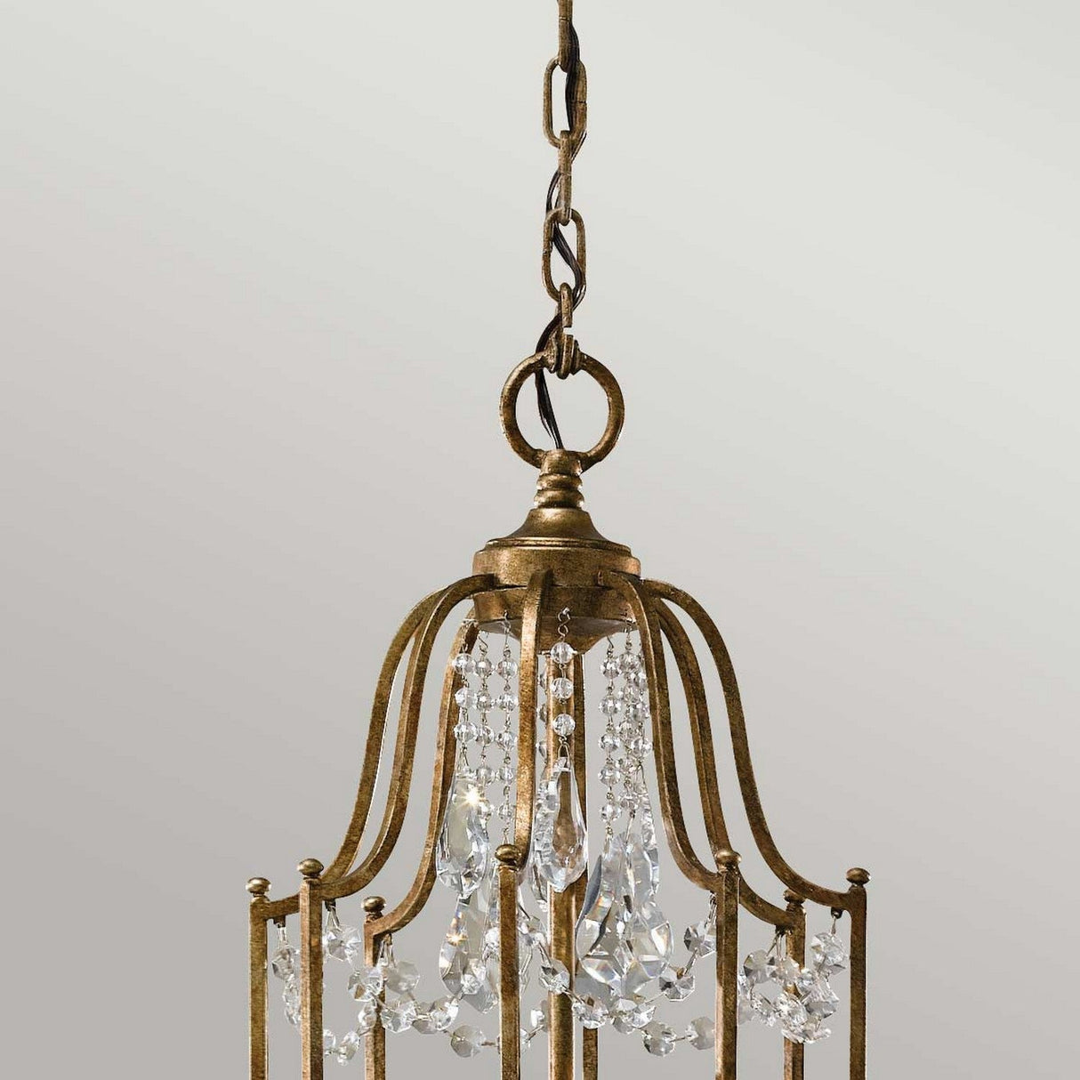 The Valentina 12 Light Chandelier - Oxidized Bronze showcases an elegant oxidized bronze finish with gold-toned metal arms. Graceful crystal teardrops and delicate crystal bobeches are beautifully suspended by a chain, complementing a light gray backdrop.