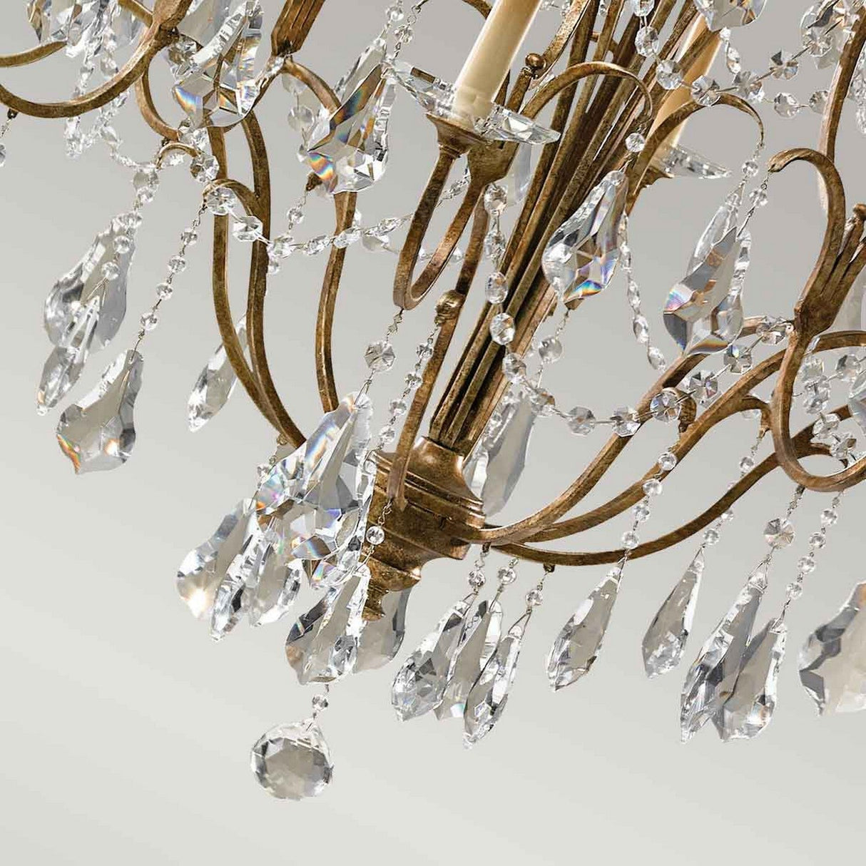 In the Valentina 12 Light Chandelier - Oxidized Bronze, teardrop-shaped crystal pendants sparkle alongside oxidized bronze metalwork, accentuated by intricate crystal bobeches, all set against a neutral background.