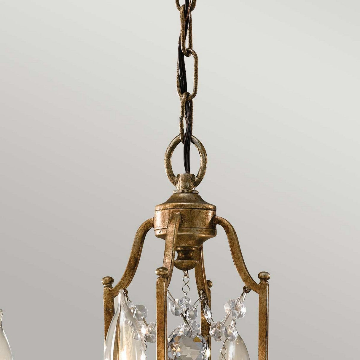 A close-up of the Valentina 4 Light Chandelier - Oxidized Bronze reveals its vintage-style allure, with intricate metalwork and crystal bobeches. The oxidized bronze fixture hangs from a chain against a neutral backdrop, emphasizing its sophisticated design.