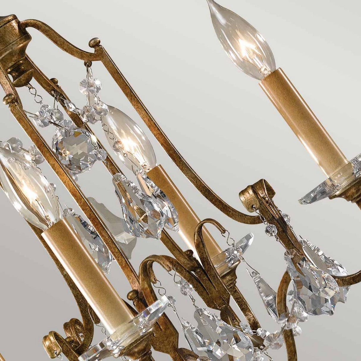 Close-up of the Valentina 4 Light Chandelier - Oxidized Bronze features candle-shaped bulbs and detailed metalwork. Crystal bobeches and accents hang beautifully, catching the light to add elegance to the design. The soft gray background complements its timeless charm.