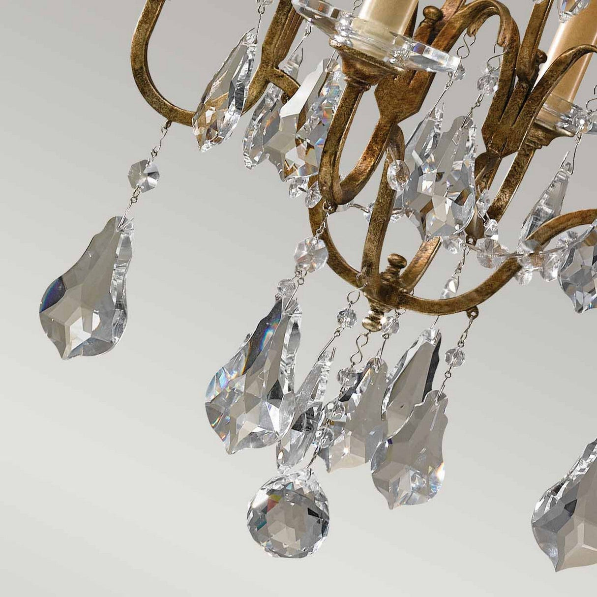 A close-up of the Valentina 4 Light Chandelier - Oxidized Bronze showcases its intricate arms adorned with oxidized bronze and highlighted by large, teardrop-shaped crystal pendants accompanied by crystal bobeches. These crystals catch and reflect light, producing a dazzling effect against a neutral background.