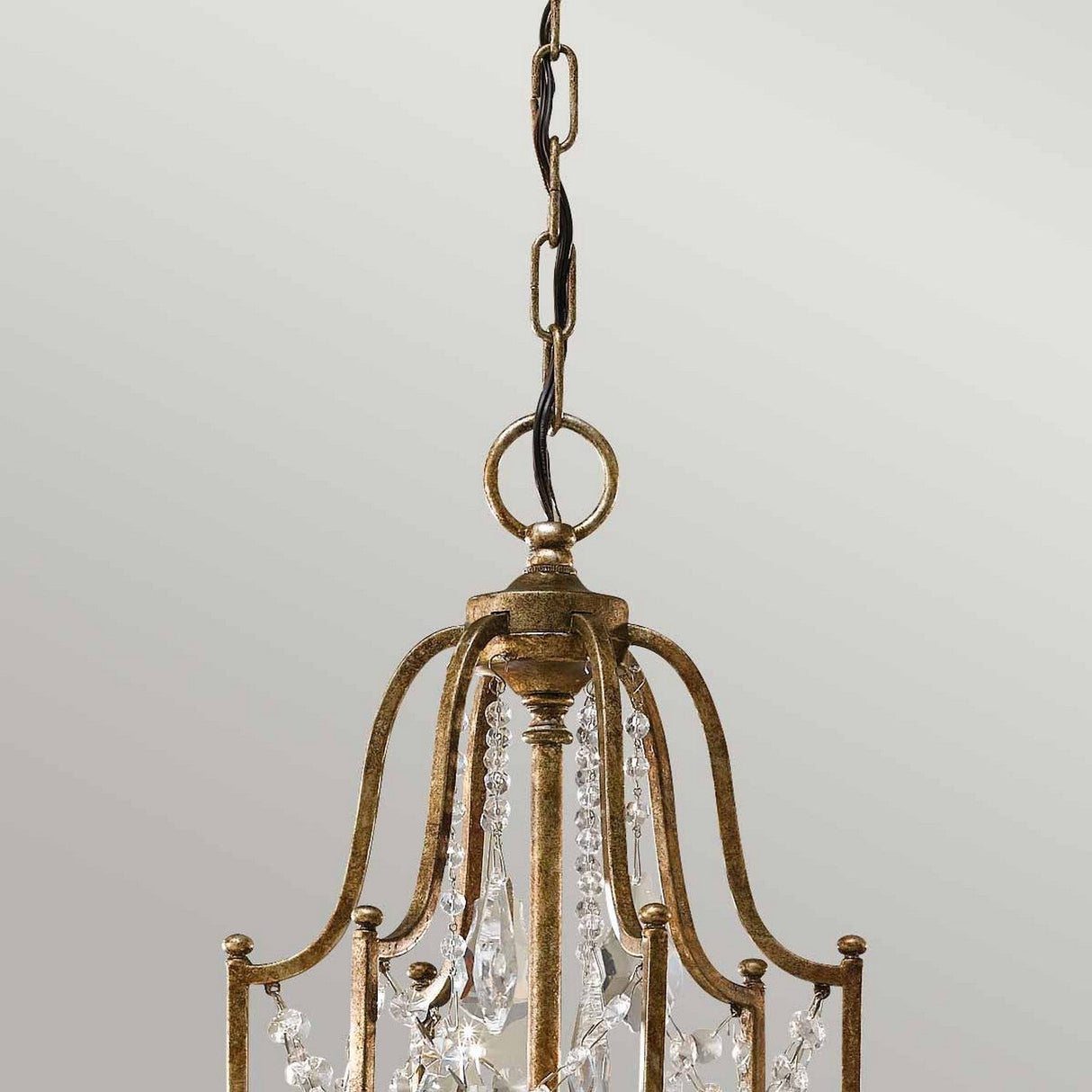 A close-up of the Valentina 6 Light Chandelier - Oxidized Bronze highlights its exquisite design with a metallic frame finished in oxidized bronze. It is adorned with polished glass crystals and suspended by a chain, adding luxury to a neutral light gray background.