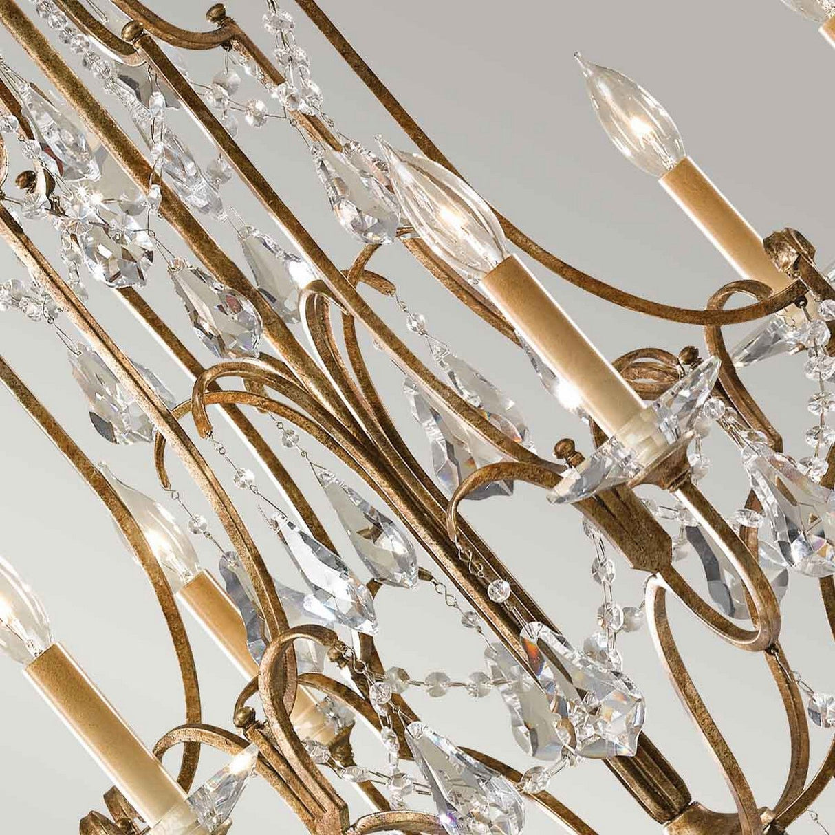 The Valentina 6 Light Chandelier - Oxidized Bronze features an intricate design with elegantly oxidized bronze arms and sparkling polished glass crystals. Its candle-style bulbs introduce a sense of luxury and sophistication against a neutral setting.