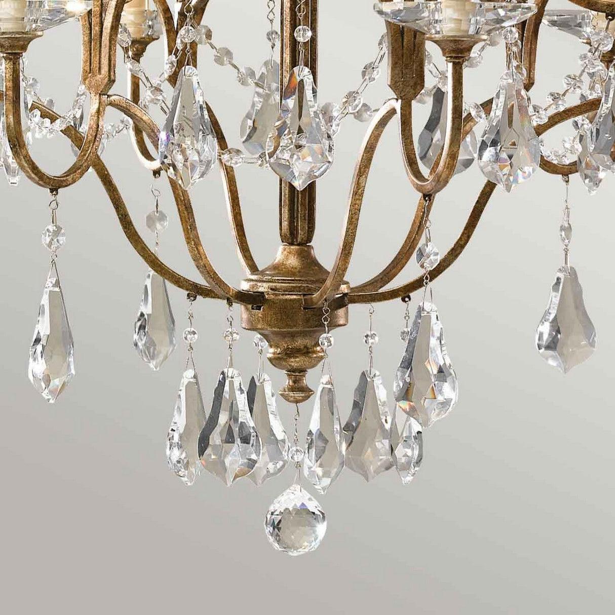 A close-up of the Valentina 6 Light Chandelier - Oxidized Bronze features its gold frame adorned with intricate, polished glass crystals cascading from its oxidized bronze arms. The crystals capture the light beautifully, producing a sparkling effect against a neutral background.