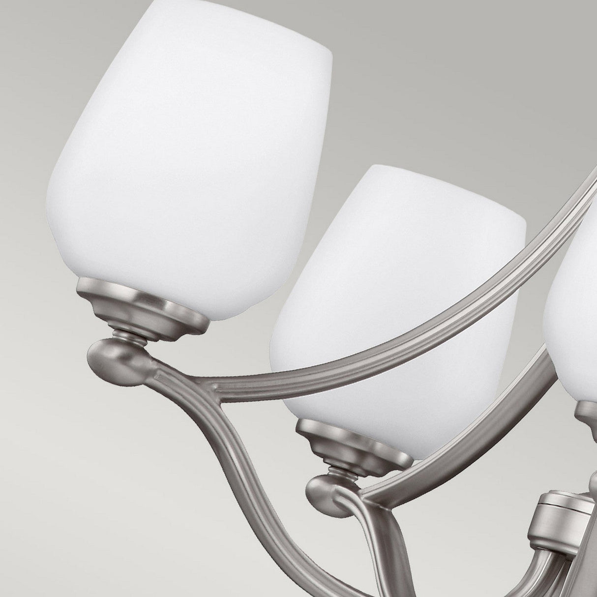 A close-up of the Vintner 5 Light Chandelier - Satin Nickel showcases its three opal etched glass shades and sleek metallic arms in a satin nickel finish against a light grey background.