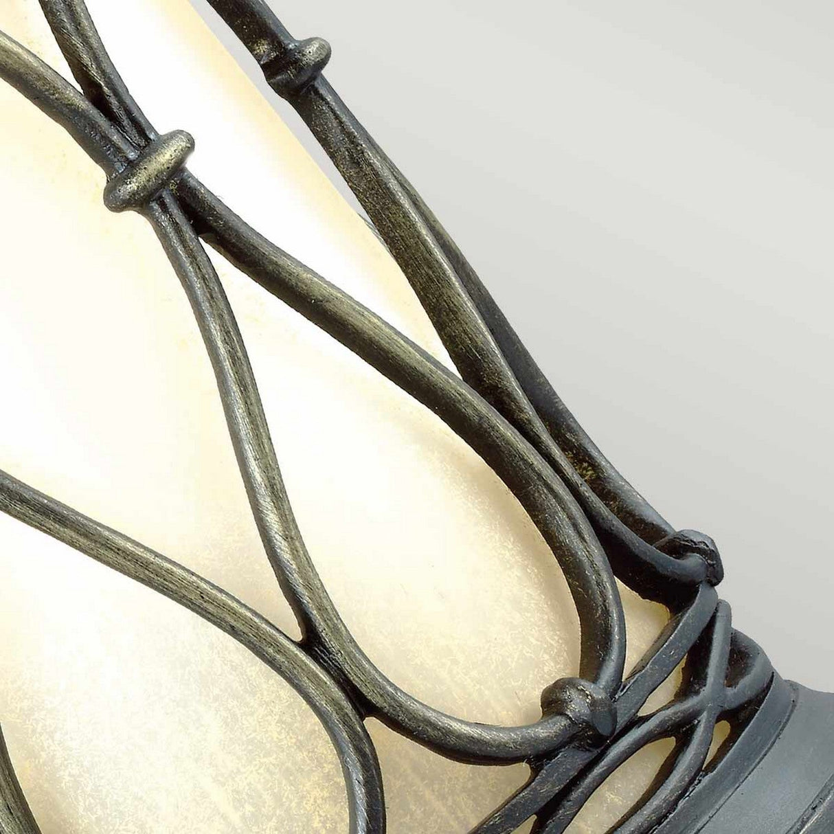 A close-up of the Wellfleet 1 Light Outdoor Wall Lantern in aged bronze showcases its decorative wrought iron detail with a curved pattern, reminiscent of contemporary design, set against a soft beige background.