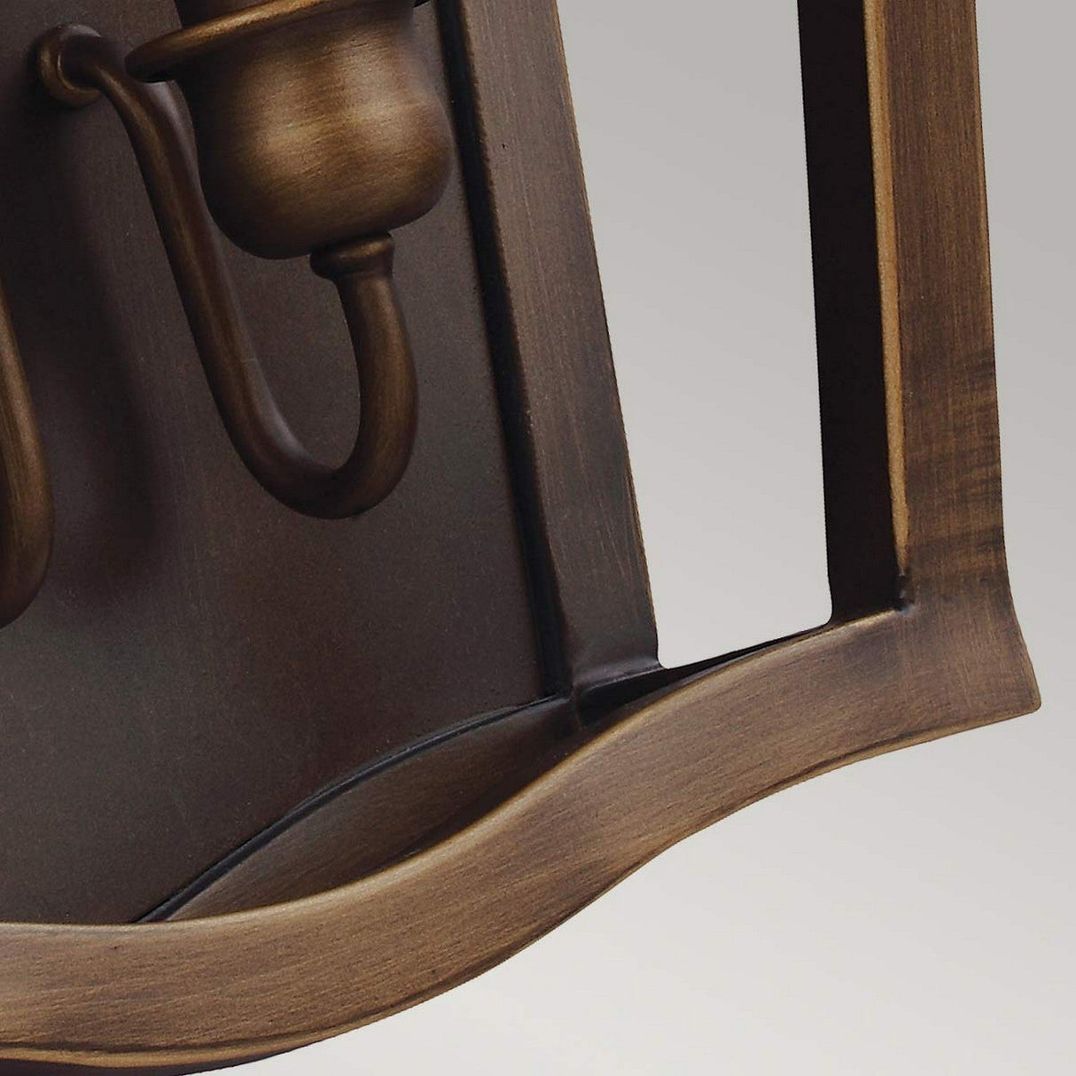 A detailed view of the Yarmouth 3 Light Wall Light in Painted Aged Brass, featuring a curved arm and wide base that harken back to traditional lantern styles, set against a plain gray background. The fixture's warm patina exudes a timeless elegance synonymous with an aged brass finish.