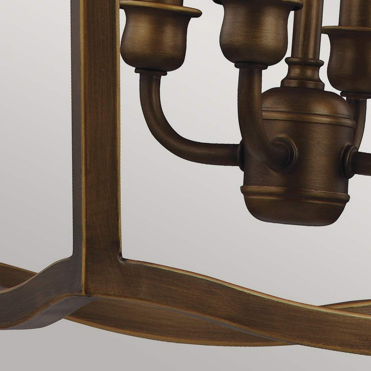 The Yarmouth 4 Light Chandelier - Painted Aged Brass showcases a close-up of its gracefully curved arms and candle-style bulb holders, set against a simple light background. This chandelier seamlessly blends classic design with elegance, offering an aesthetic that is both timeless and modern.