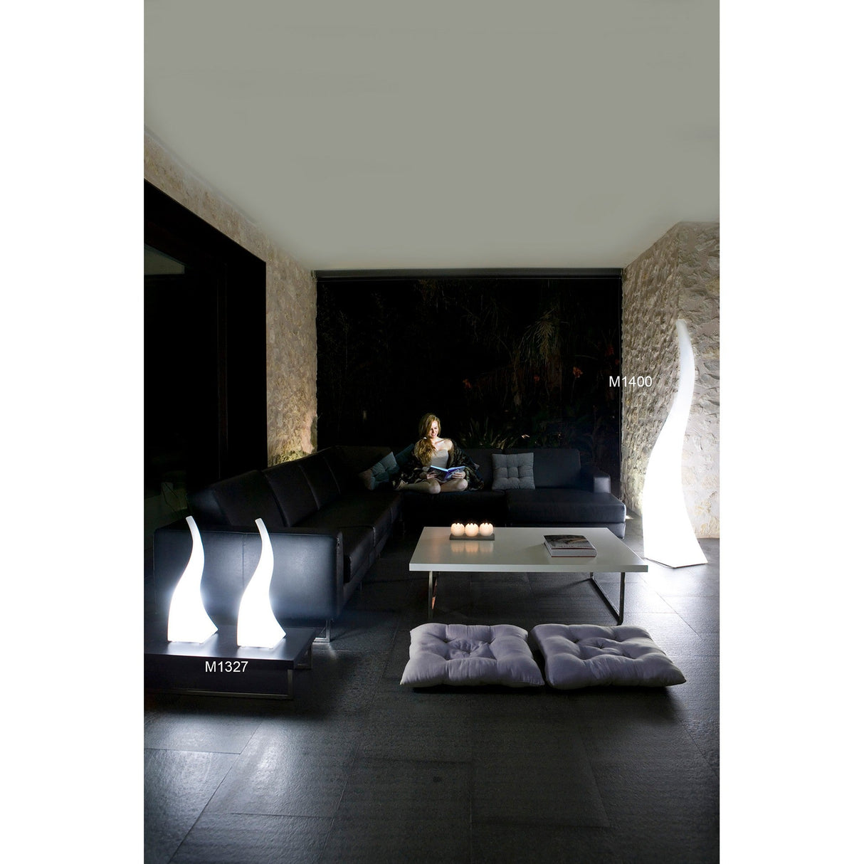 A woman sits on a couch in a room accented by the Flame 5 Light Outdoor Floor Lamp in Opal White, adding a sleek and stylish touch to the contemporary space.