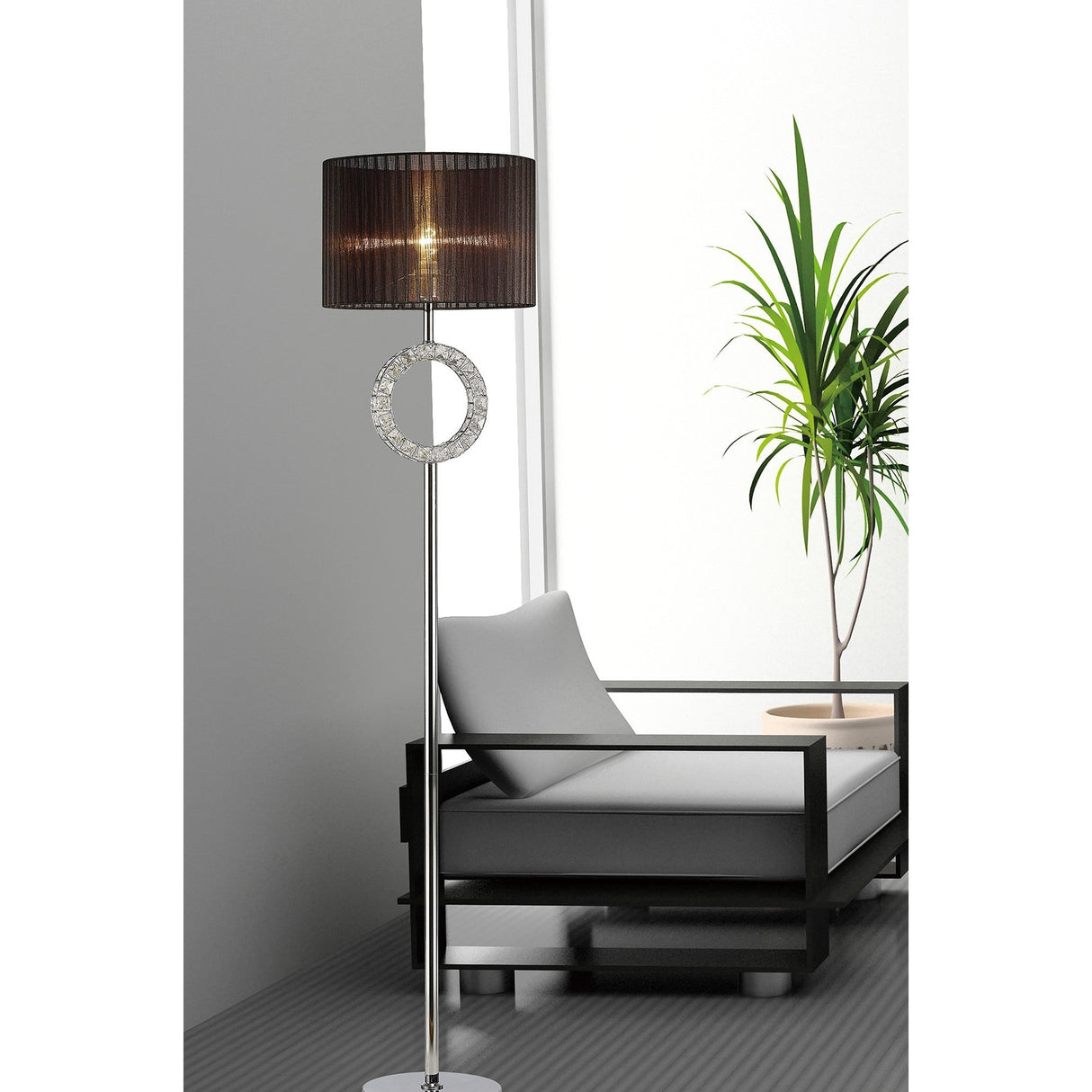 A modern living room with the Florence Round 1 Light Crystal Floor Lamp in chrome and white shade featuring a circular accent, beside a black-framed lounge chair with light cushions and a tall green plant by a large window for freshness.