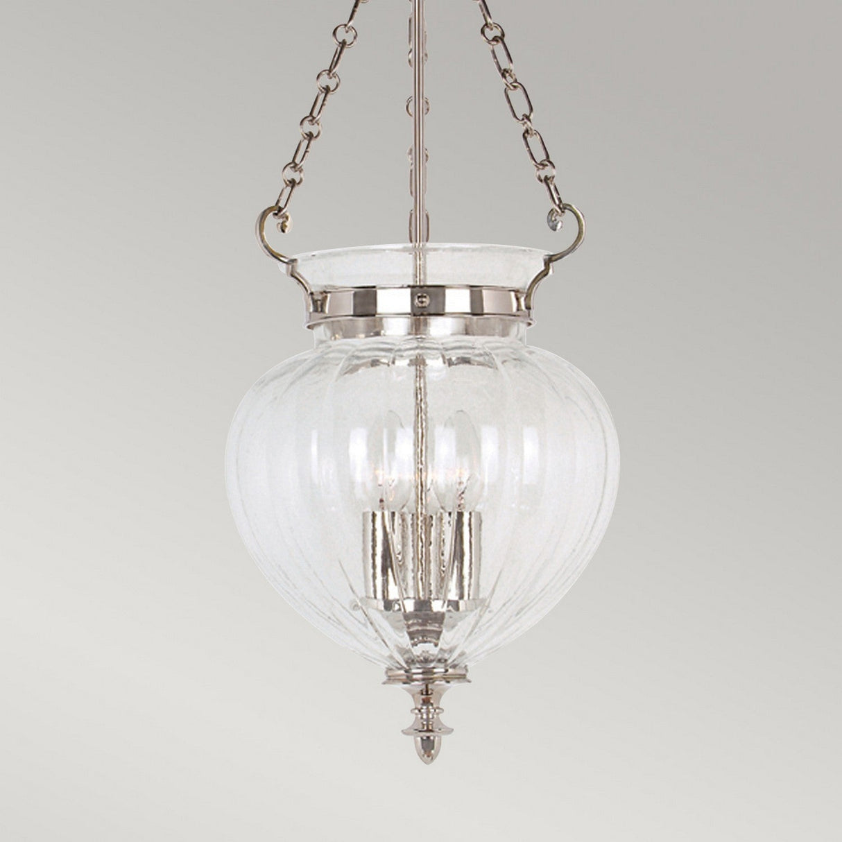 The Finsbury Park 3 Light Medium Chandelier in Polished Nickel showcases an elegant, ribbed glass design that hangs from a sleek nickel chain fixture. Inside, the chandelier features multiple candle-style lights for a classic touch against the neutral gray background.