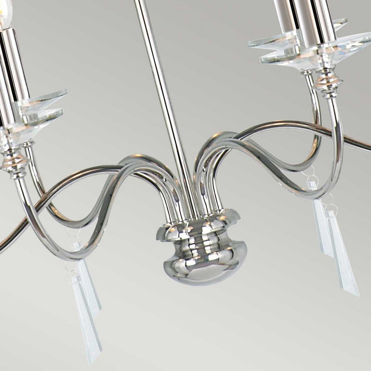 A close-up of the Finsbury Park 6 Light Chandelier - Polished Nickel reveals its elegant curved arms and candle-shaped light fixtures. This chandelier, featuring hand-cut glass accents, is displayed against a light gray background.