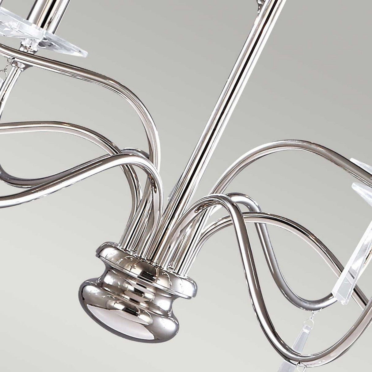 Close-up of the Finsbury Park 9 Light Chandelier - Polished Nickel, featuring curved metallic arms and candle-like light fixtures. Its polished nickel finish provides an elegant, contemporary appearance, enhanced by hand-cut glass accents that shimmer against a neutral background.