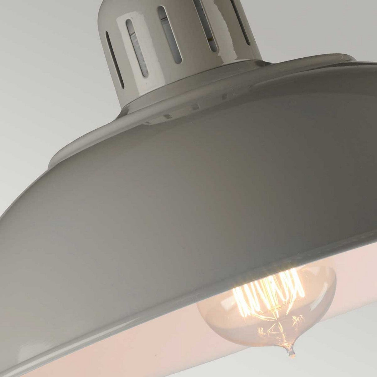 This close-up features a stylish pendant light equipped with a vintage-style bulb, ideal for focused task lighting. A glossy white metal shade complements the bulb's warm glow, while vent-like cutouts on top contribute a retro-industrial flair. This design harmonizes seamlessly with its modern aesthetic, reminiscent of the Franklin Desk Lamp - Grey.