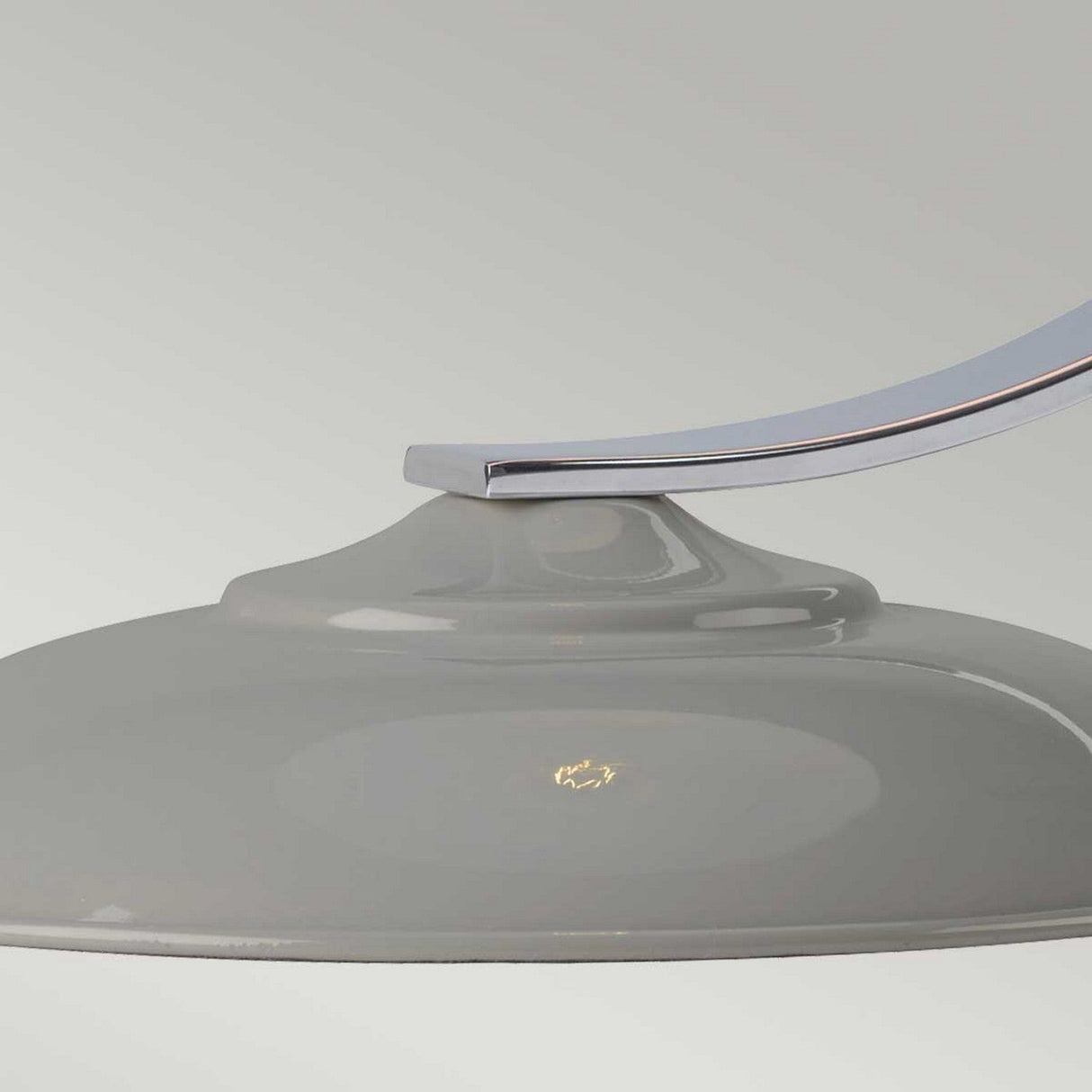 Close-up of a dome-shaped light fixture in a glossy gray finish. This elegant Franklin Desk Lamp - Grey, mounted on a gracefully curved metal arm against a soft light gray background, exemplifies modern style. The directed task lighting highlights a small emblem on the surface of the fixture.