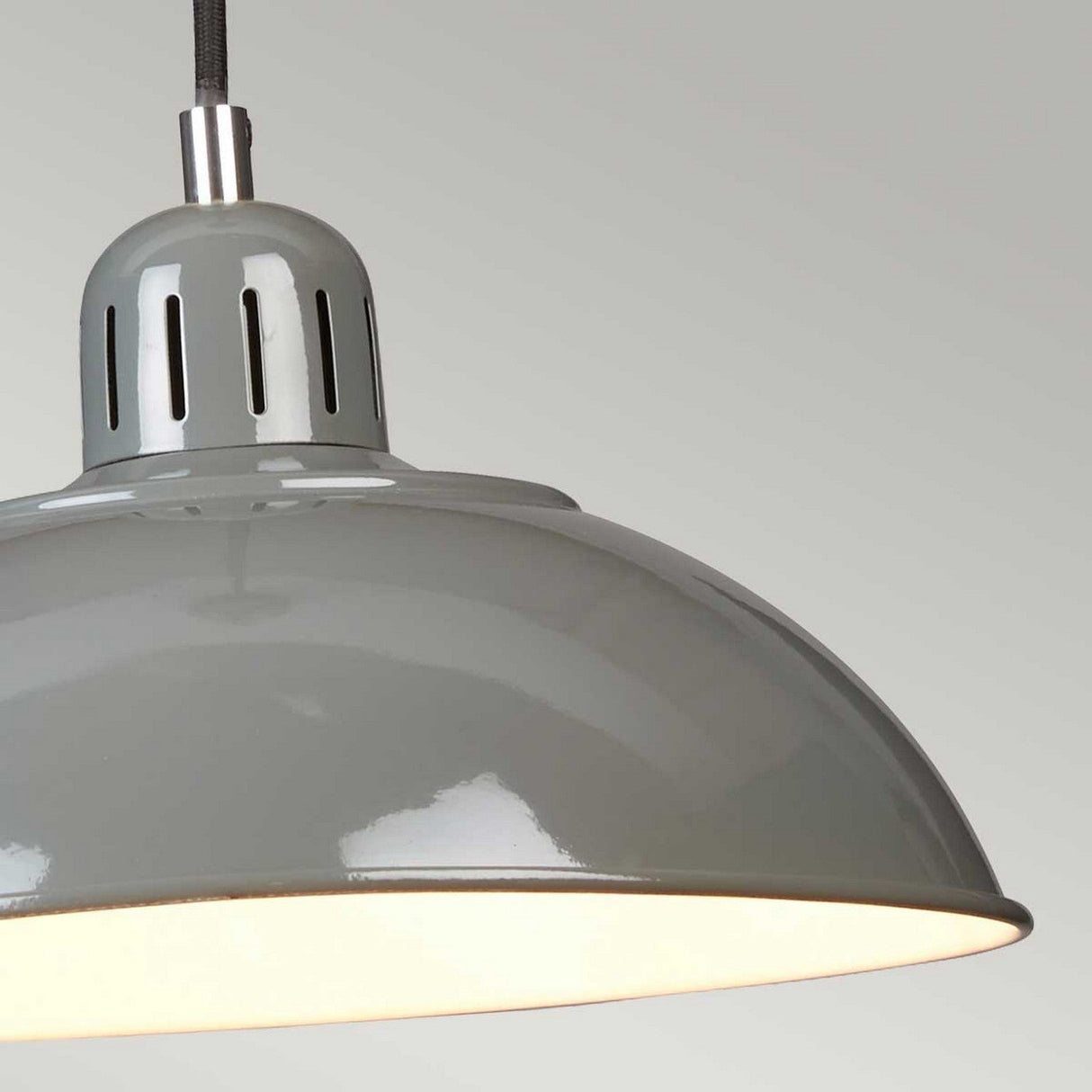 A close-up of the Franklin Pendant Light - Grey, featuring an industrial-style metal design with a sleek, shiny finish. The light is illuminated, casting a warm glow that evokes retro diner vibes, and is set against a plain, light gray background.