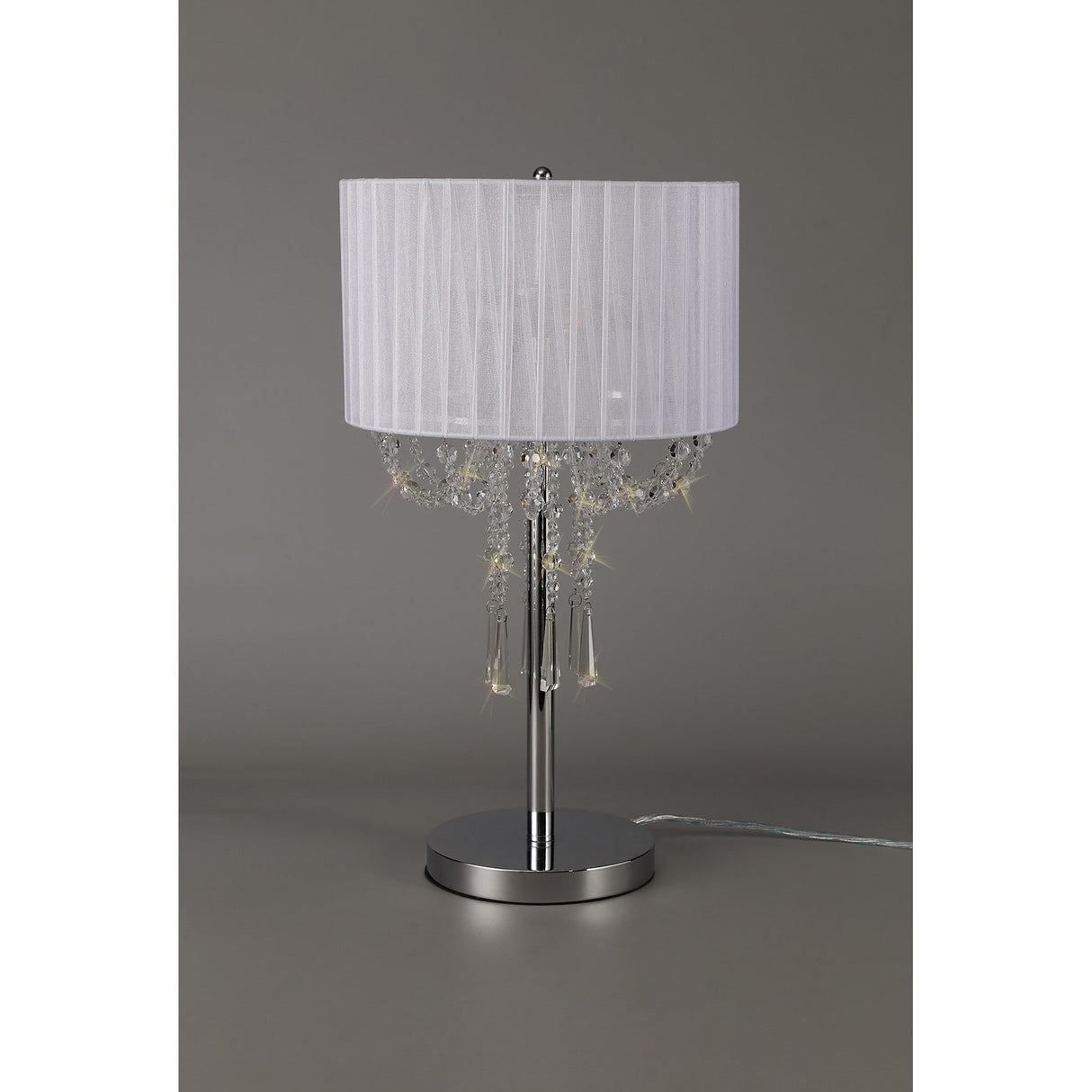The Freida 3 Light Crystal Table Lamp features a polished chrome frame, white pleated fabric shade, and hanging crystal bead accents, beautifully showcased against a plain gray background.