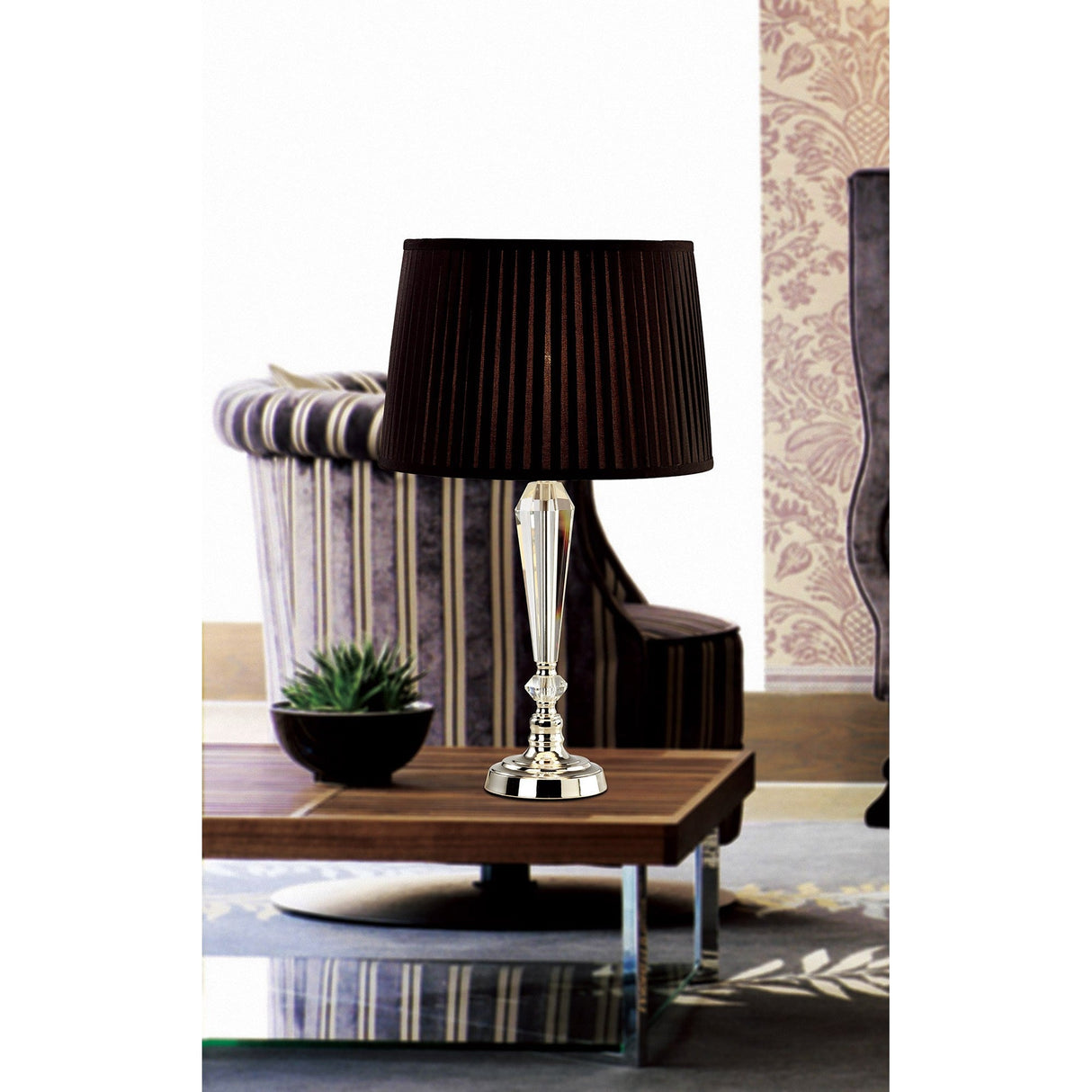 The Freya 1 Light Crystal Table Lamp - Silver Without Shade sits on a wooden coffee table near a small potted plant, with a striped armchair and floral wallpaper in the background.