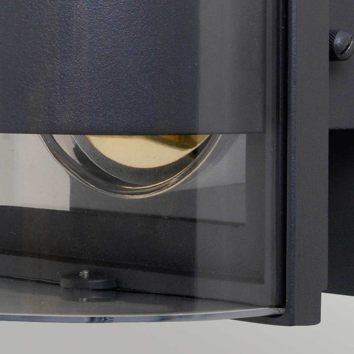 Close-up of the Frida Outdoor Small Wall Light in graphite, crafted from die-cast aluminum. It features a round glass cover with a visible bulb and boasts an IP54 rating, all set against a light gray background.