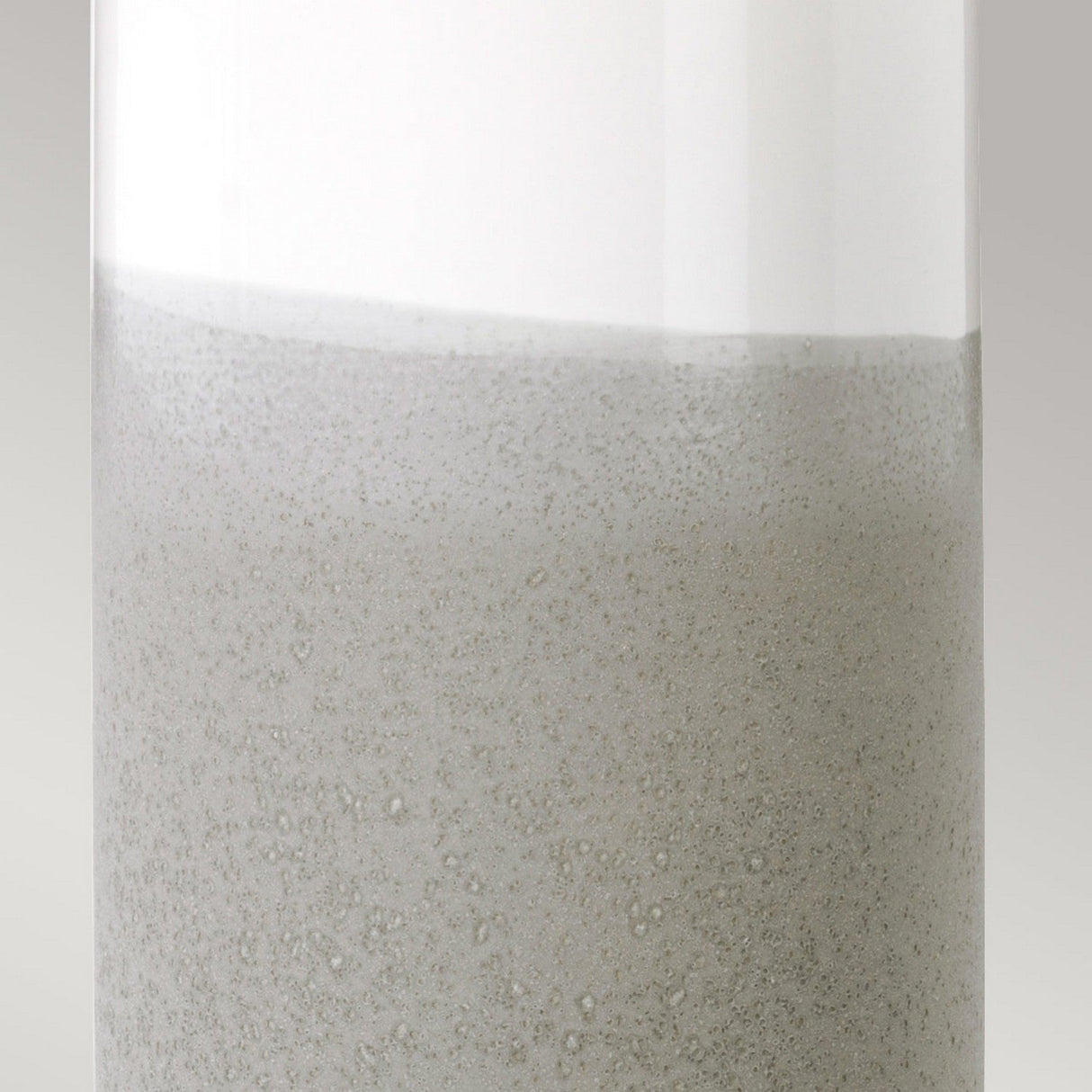 Close-up image of a Fulwell 1 Light Table Lamp in White Gloss and Matt Grey, featuring a glass container filled with a light gray liquid. The liquid's surface is akin to a delicate emulsion with tiny bubbles, resembling the lamp's modern textured design. The neutral and plain background enhances its contemporary feel.