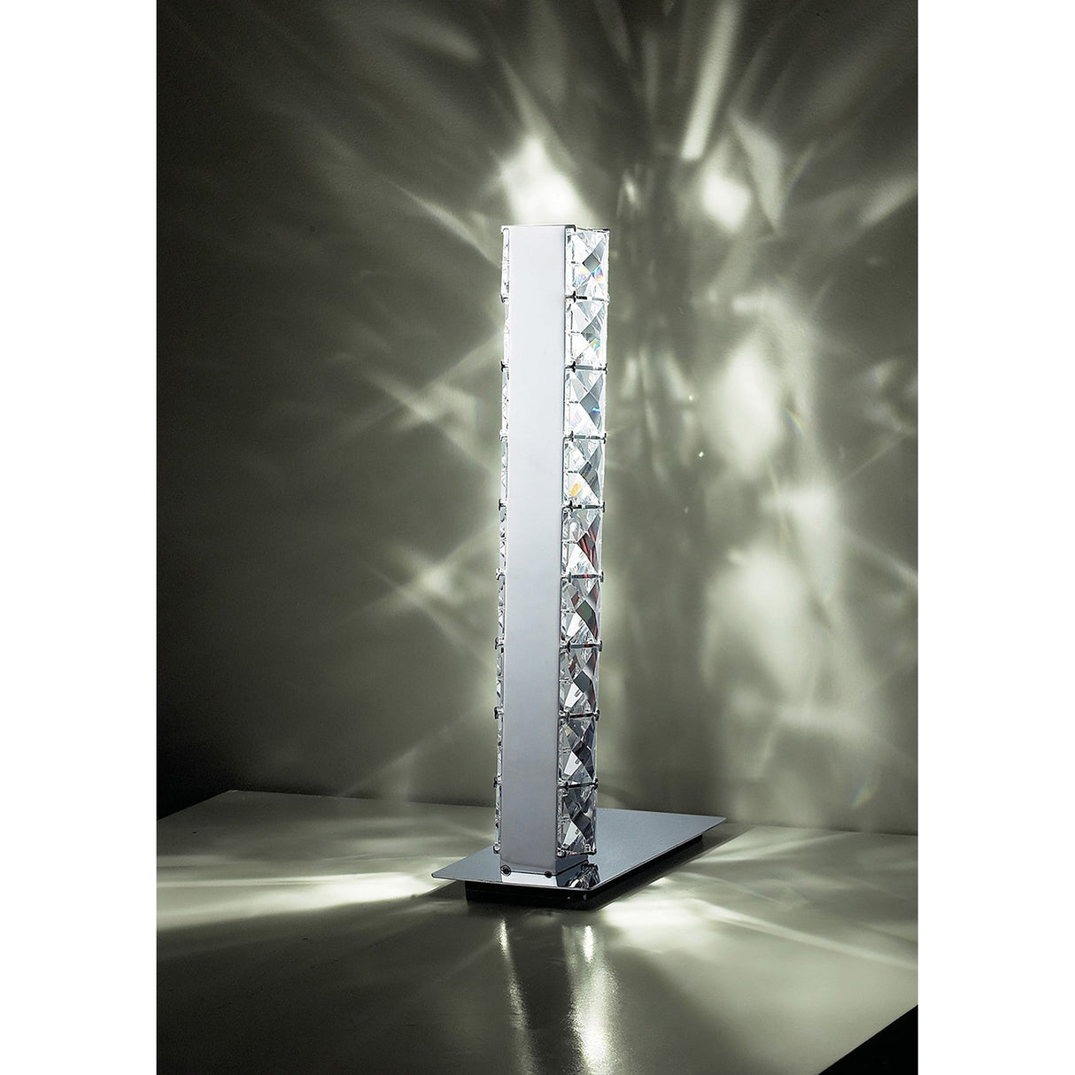 The Galaxy LED Crystal Table Lamp 3W 6000K in Polished Chrome features geometric crystal accents that emit bright light and cast starburst patterns, all elevated by a sleek rectangular base for a modern decorative touch.