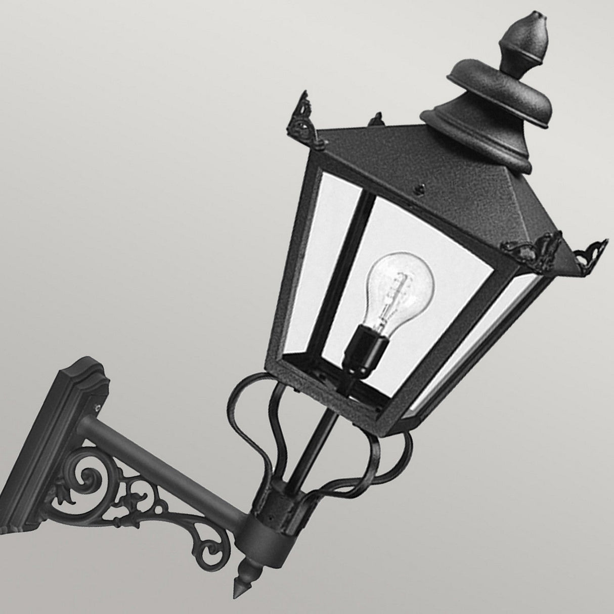 The Grampian 1 Light Outdoor Wall Lantern - Black showcases ornate metalwork and a visible bulb, crafted from cast aluminum with a Victorian-inspired design, beautifully contrasted against a plain, light gray background.