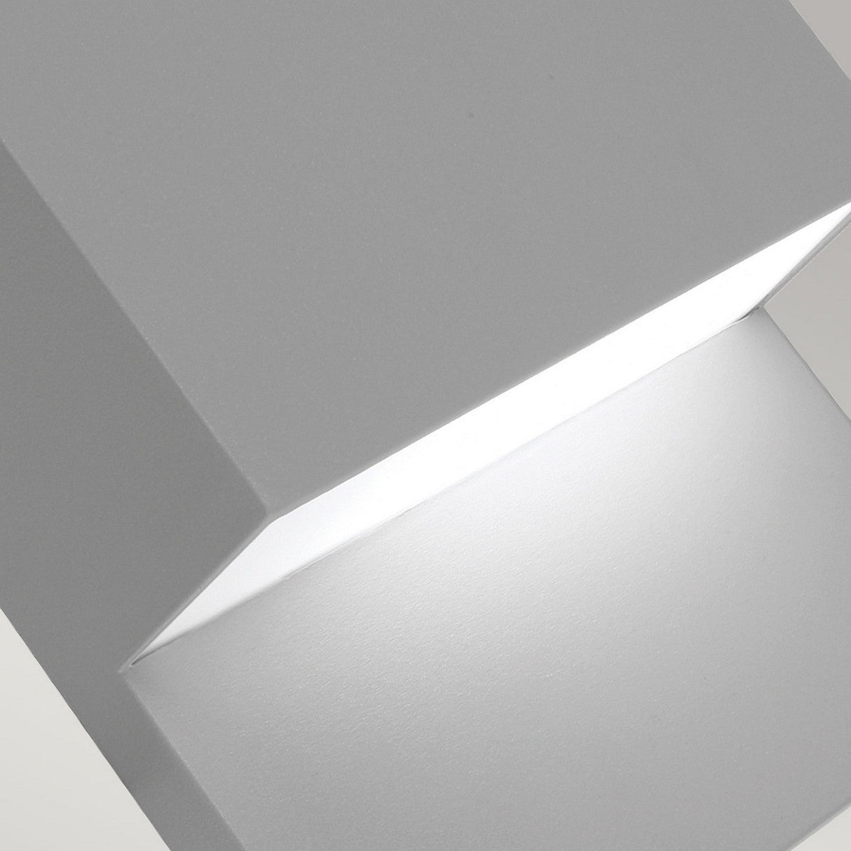 Close-up of the Geneve Outdoor 1 Light Wall Lantern in its modern, minimalist form, crafted from die-cast aluminium with a geometric design. The light softly illuminates the surface below, casting a subtle glow on the neutral-colored wall.