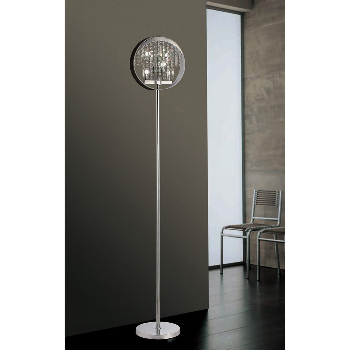 The Geo 9 Light Crystal Floor Lamp in chrome with a black shade stands on a dark floor near a gray wall; two metal chairs by the large window enhance the room’s modern glamour with stylish, reflective lighting.