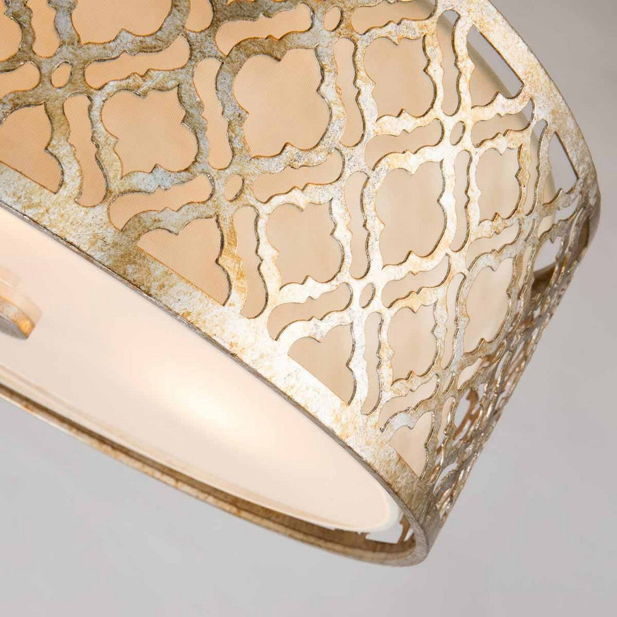 A detailed view of the Arabella 3 Light Duo-Mount Large Pendant/Semi-Flush reveals its elaborate metallic structure featuring a geometric design. It flaunts a gold finish with an ivory shade, giving it an aged look that radiates a warm glow through its intricate lattice openings.