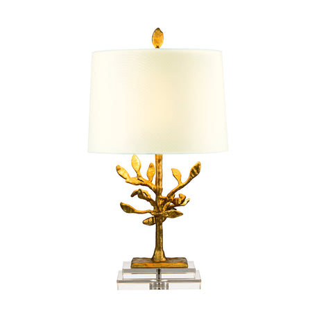The Audubon Park 1 Light Table Lamp – Gold features a white cylindrical shade and a gold-toned base crafted from cast metal, designed to resemble an abstract tree or branch structure. It gracefully rests on a transparent rectangular platform, mirroring its intricate tree motif.