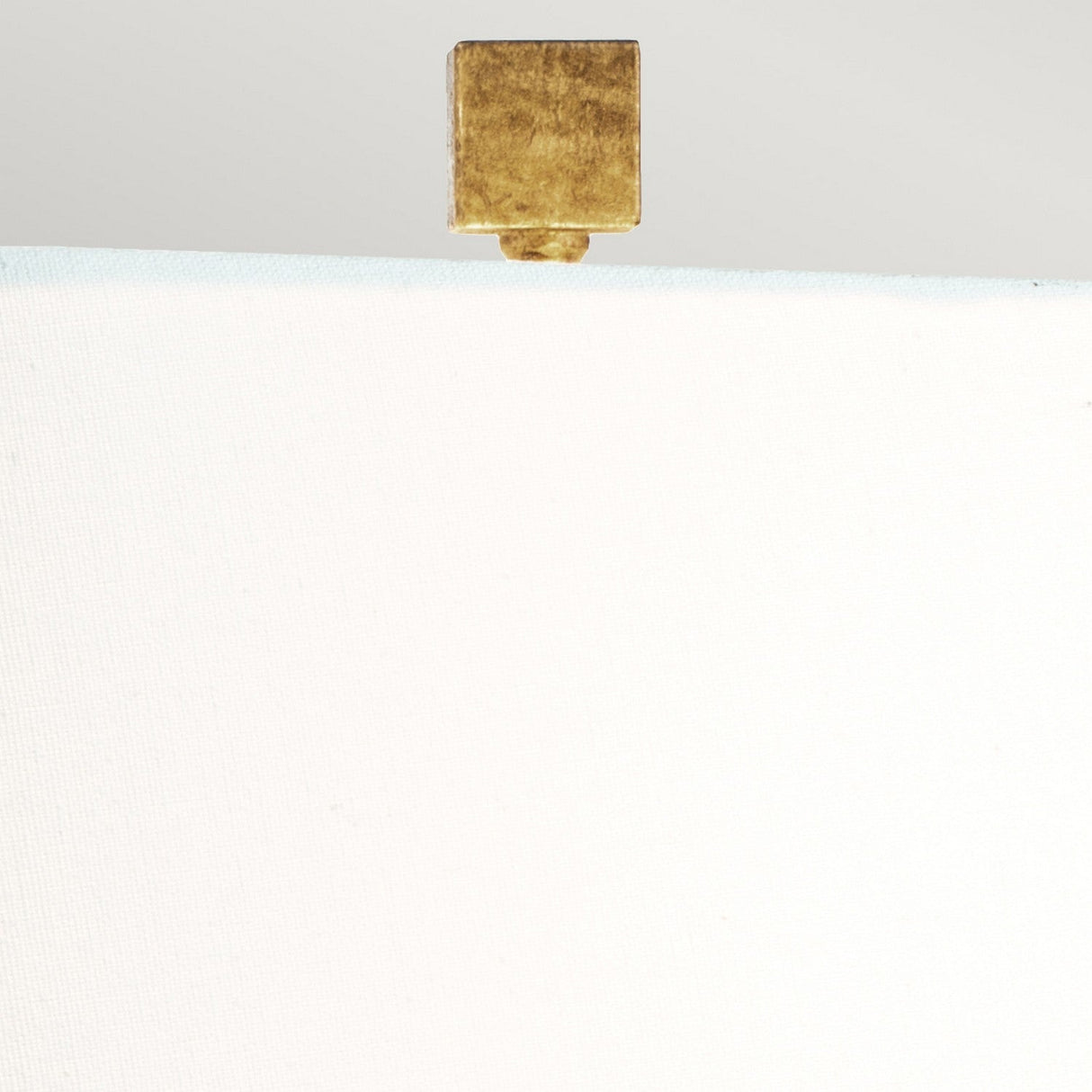 A gold cube-shaped clip holds a white canvas, evoking the refined simplicity of the Jackson Square 1 Light Table Lamp - Gold with its cream linen shade against a light gray background.