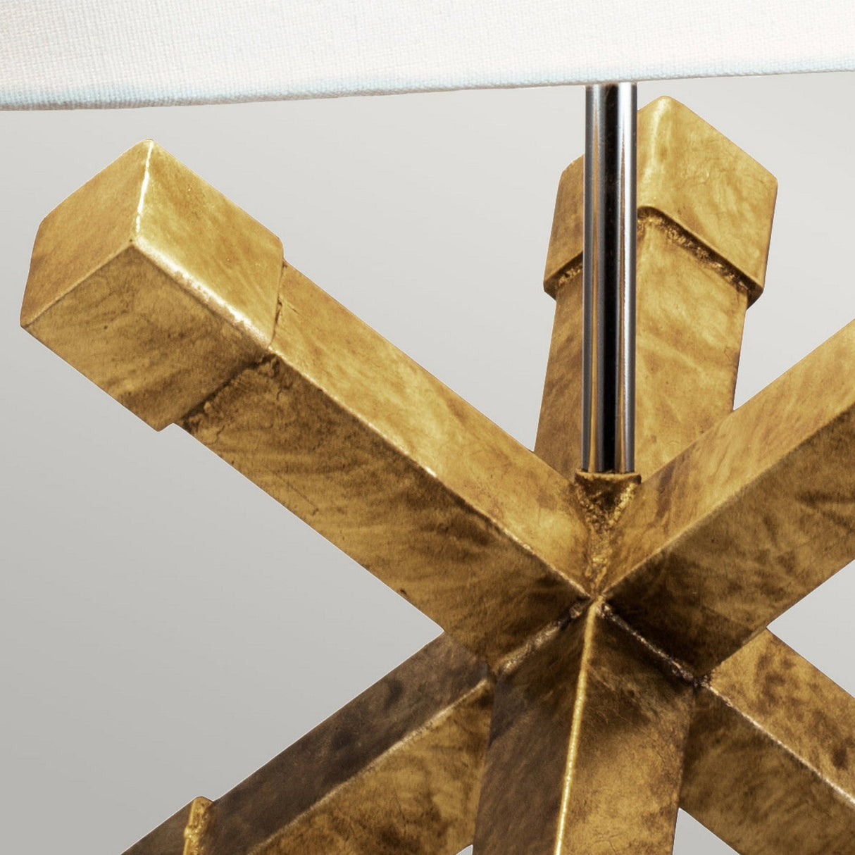 Close-up of the Jackson Square 1 Light Table Lamp - Gold, highlighting its metallic, gold-toned geometric base with intersecting beams. The upper part of its cream linen shade is visible against a neutral background.